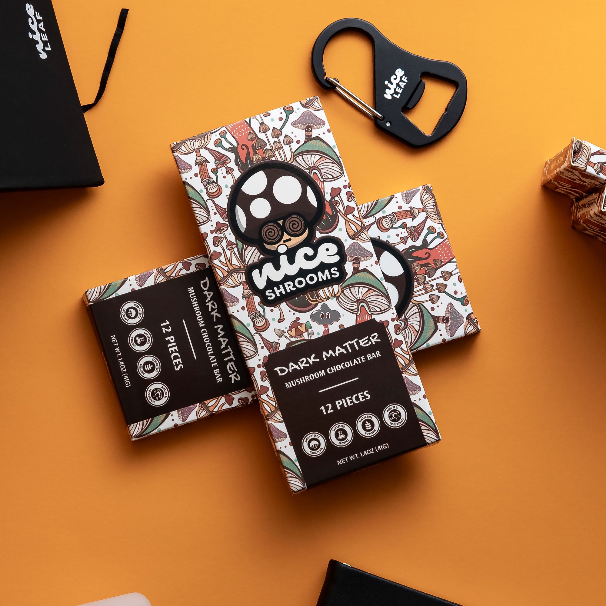 Three boxes of 'Nice Shrooms' Dark Matter Mushroom Chocolate Bar arranged on a bright orange background, alongside a black bottle opener and a black gift box.